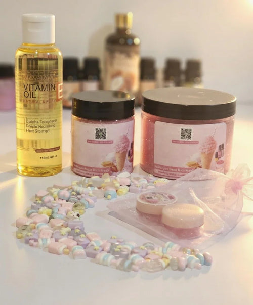 Bubble gum body scrub jars, vitamin E oil, pastel beads, and skincare products on white background